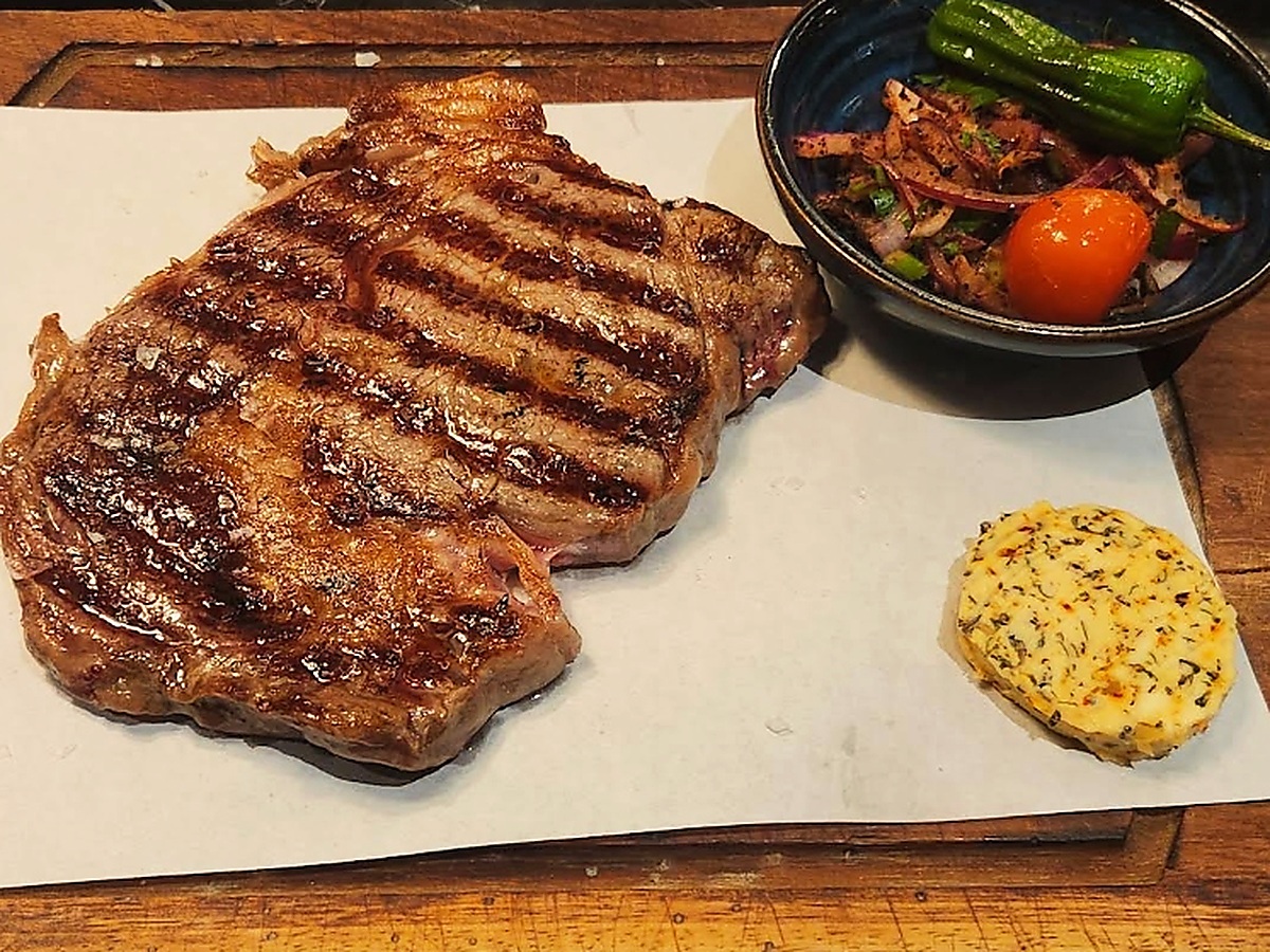 Babalar Grill Spezial: Antrikot 300 g (Saftig gegrilltes Entrecôte) mit Kräuterbutter und Sumach-Zwiebeln auf dem Holzbrett