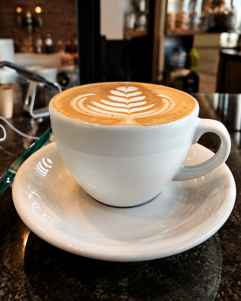 Rosetta-Latte-Art in klassischer weißer Keramiktasse auf dunklem Naturstein