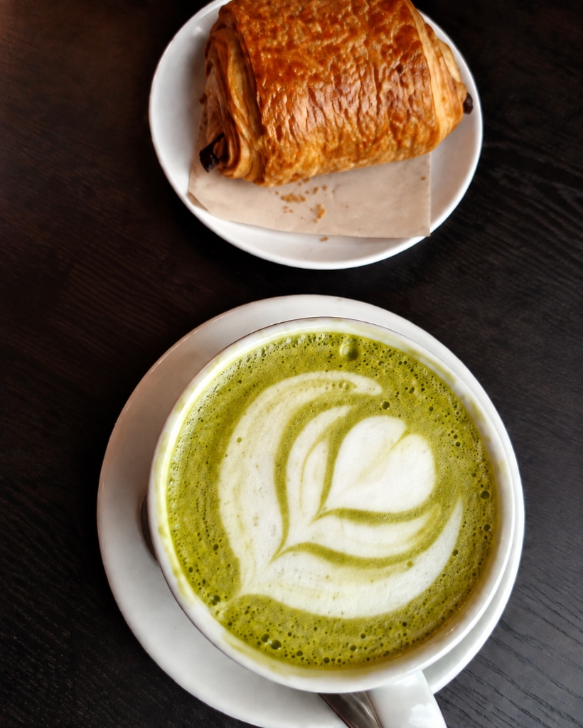 Matcha und Pain au Chocolat auf dem dunklen Holztisch